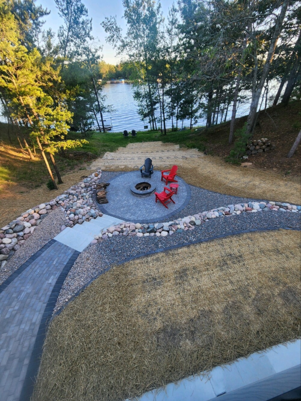Aerial view of pavers, firepit, chairs, and a lake in the background.