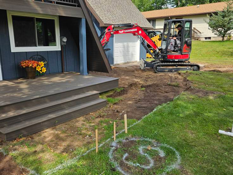 Mini excavator grading the ground in front of an A-frame home during a paver installation project in Nekoosa, Wisconsin