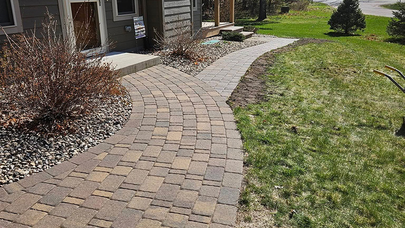 Curved paver walkway leading to a home's front entry with decorative gravel garden bed alongside