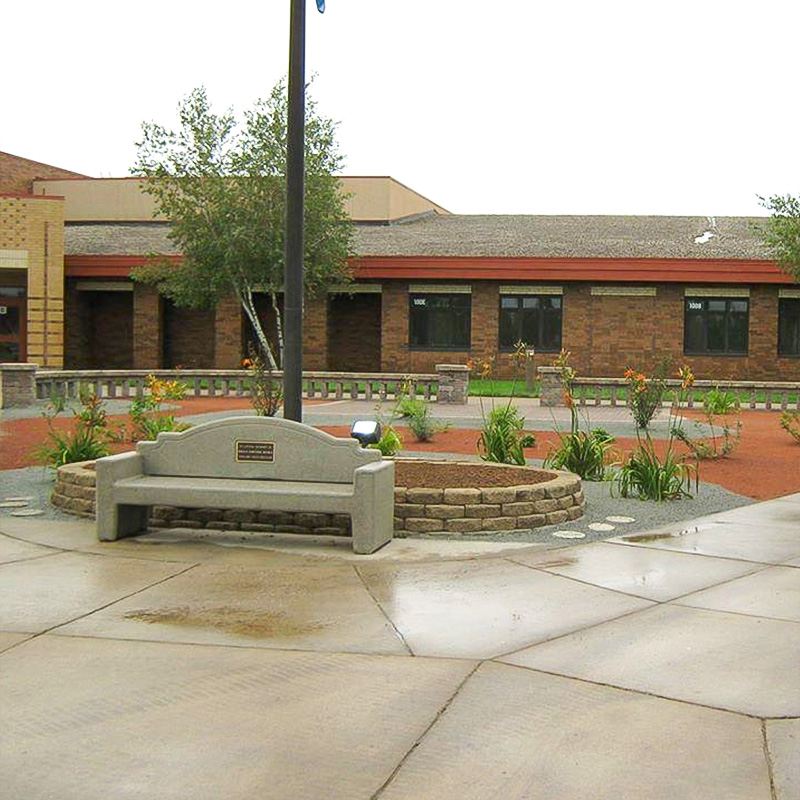 Commercial courtyard with a decorative stone planting bed, concrete bench, perennial plantings, and brick paver walkways