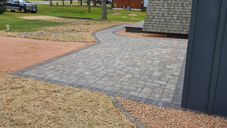 Newly installed paver walkway with a dark soldier course border and fresh straw covering surrounding seeded areas