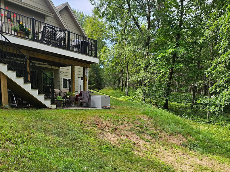 Wooded residential backyard with a raised deck and sloped lawn before landscaping in Nekoosa, Wisconsin