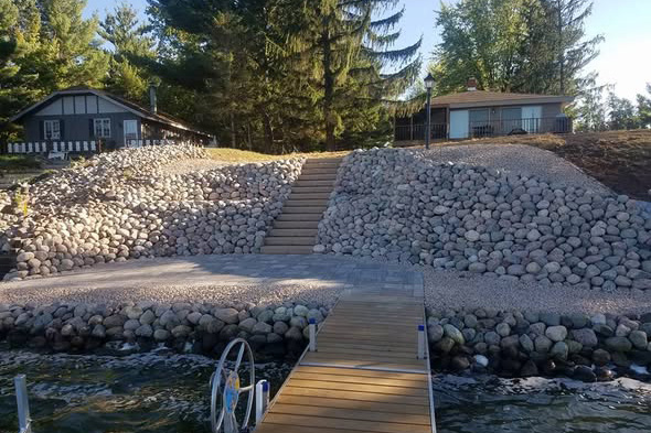 Large boulder shoreline with paver steps leading up from a boat dock to a lakefront property