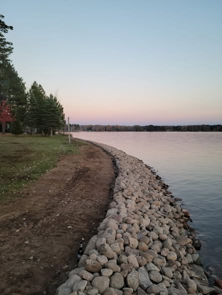 Boulder shoreline riprap installation along a lakefront property at dusk