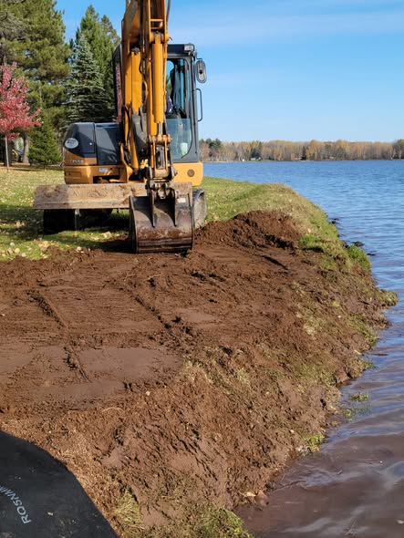 Excavator grading a lakefront bank in preparation for shoreline erosion control installation