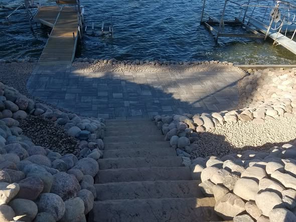 Paver steps leading down to a lakefront dock with round boulder edging and gravel shoreline detail