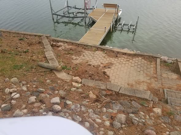 Lakefront before photo showing an unfinished shoreline with rough paver landing and erosion along the bank leading to a boat dock