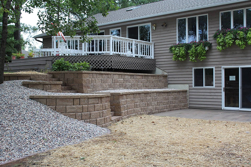 Tiered concrete block retaining walls with built-in steps, gravel area, and freshly seeded yard beside a residential deck