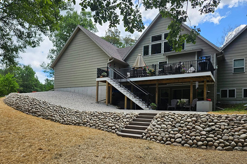 Completed round boulder retaining wall with paver steps and gravel area beneath a raised deck after landscaping