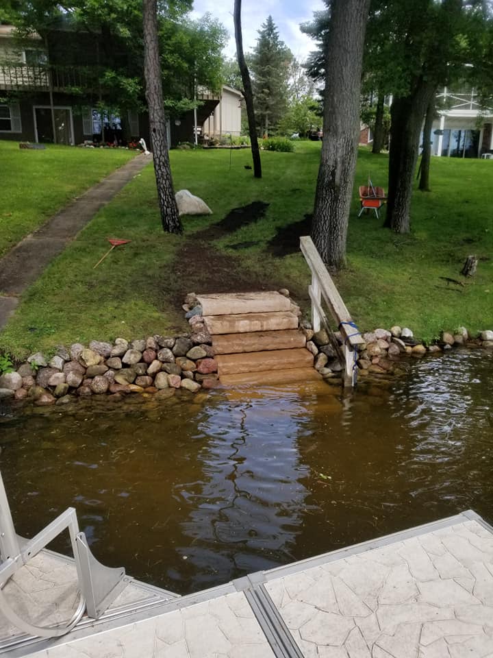 Aging timber and rock shoreline steps leading to a lakefront dock before renovation