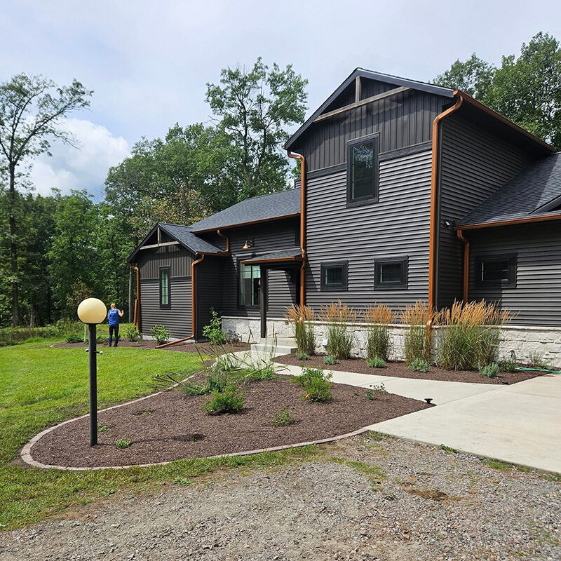 New construction home with freshly installed foundation plantings, ornamental grasses, dark mulch beds, and a globe pathway light